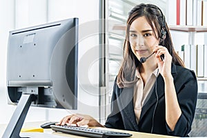 Smiling friendly asian female call-center agent with headset working on support hotline in the office