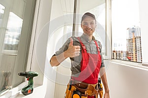 Smiling friendly builder wearing a tool belt working with a drill in a new house under construction with copy space