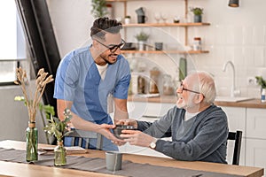 Smiling friendly caretaker serving breakfast to a pensioner