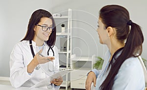 Smiling friendly female doctor discusses diagnosis with woman and makes notes in clipboard.