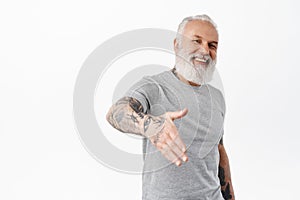 Smiling friendly mature man with tattoos give hand for handshake and laughing, nice to meet you gesture, meeting someone