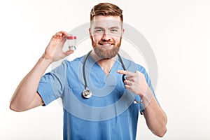 Smiling friendly pharmacist pointing finger at bottle with tablets