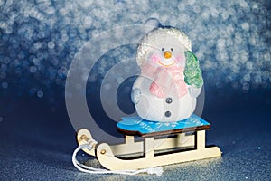 Smiling friendly snowman figure on a sleigh. Cute Christmas toy on a shiny blue background. Copy Space