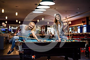 Smiling friends with cues playing billiard in pub