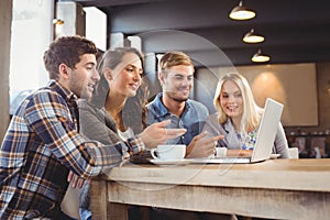 Smiling friends drinking coffee and pointing on laptop screen