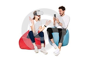 Smiling friends experiencing virtual reality glasses seated on beanbags isolated on white background. photo