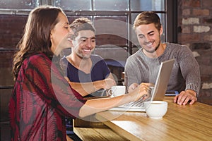 Smiling friends having coffee together and looking at laptop