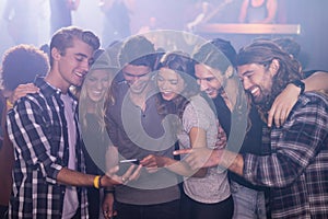 Smiling friends looking at smart phone in nightclub