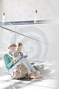 Smiling friends reading book while sitting on corridor at university