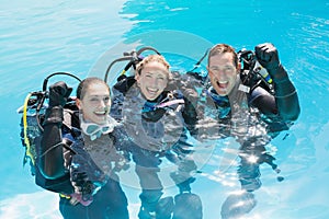 Smiling friends on scuba training in swimming pool cheering at camera