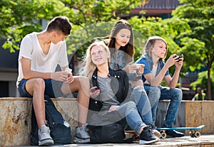 Smiling friends sitting with mobile phones in park