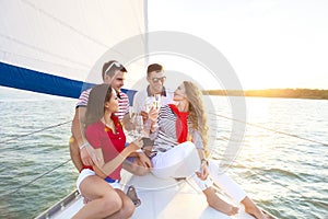 Smiling friends sitting on yacht deck and greeting drinking champagne