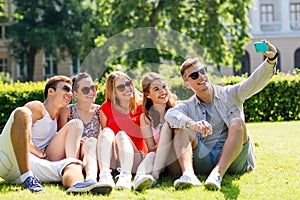 Smiling friends with smartphone sitting on grass