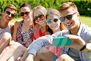 Smiling friends with smartphone sitting on grass