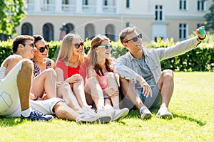 Smiling friends with smartphone sitting on grass