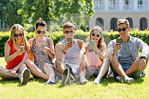 Smiling friends with smartphones sitting on grass