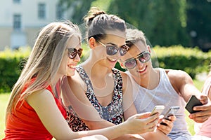 Smiling friends with smartphones sitting in park