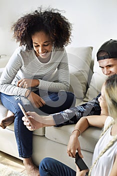 Smiling friends using smartphone together at home