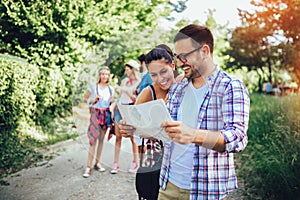 Smiling friends walking with backpacks in woods - adventure, travel, tourism, hike and people concept