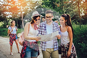 Smiling friends walking with backpacks in woods - adventure, travel, tourism, hike and people concept