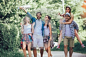 Smiling friends walking with backpacks in woods - adventure, travel, tourism, hike and people concept