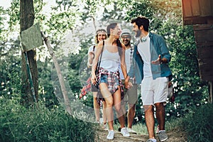 Smiling friends walking with backpacks in woods - adventure, travel, tourism, hike and people concept