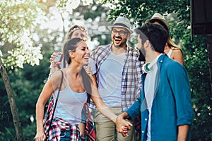 Smiling friends walking with backpacks in woods - adventure, travel, tourism, hike and people concept