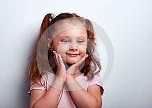 Smiling fun kid girl looking holding the hands near the face on empty copy space studio blue background. Closeup