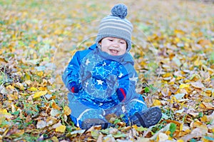 Smiling funny baby boy sitting on yellow leaves in autumn