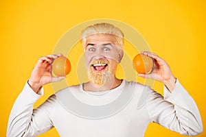 Smiling funny man with oranges in hands. Handsome young man hold fresh natural orange. Man enjoying fruit refreshment