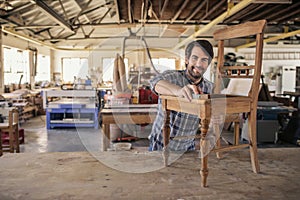 Smiling furniture maker sanding a chair in his woodworking shop