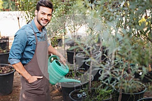 Smiling gardener in apron with watering can watering plants in garden