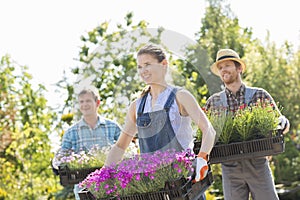 Smiling gardeners carrying crates with flower pots at plant nursery