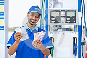 Smiling gas filling station attendant counting money at petrol pump - concept of business profit, earnings, salary and
