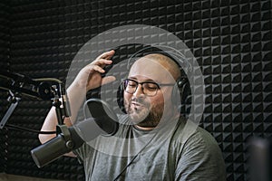 Smiling and gesturing radio host with headphones on his head reading news from paper into studio microphone on radio station