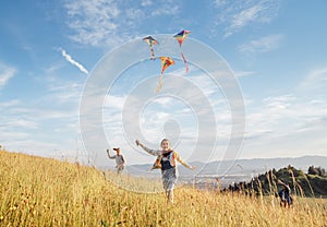 Smiling gils and brother boy with flying colorful kites - popular outdoor toy on the high grass meadow in the mountain fields.