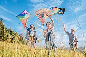 Smiling gils and brother boy running with flying colorful kites on the high grass meadow in the mountain fields. Happy childhood