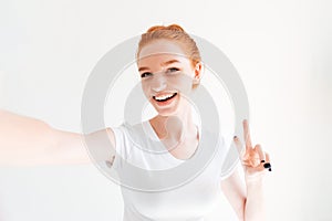 Smiling ginger woman in t-shirt making selfie and showing peace