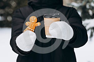 Smiling gingerbread man and paper cup of coffee in hands on blurred background.