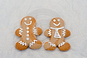 Smiling gingerbread man with sugar, spices, and vintage rolling pin on rustic, textile linen background.