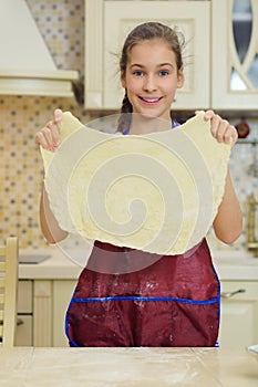 Smiling girl in apron keeps dough for pizza photo