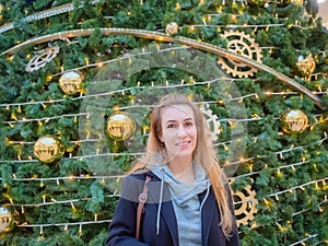 Smiling girl on the background of a large Christmas tree decorated with a garland and golden balls