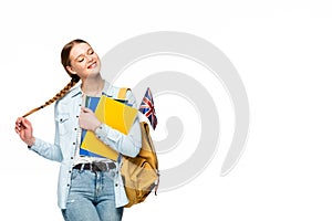 Smiling girl with backpack holding copybooks and uk flag and touching braid