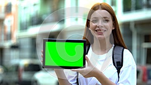 Smiling girl with backpack showing green screen tablet, cheap tours and flights