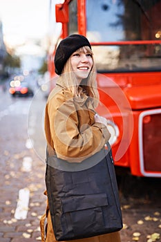 Smiling girl in beret and trench outdoor with red bus