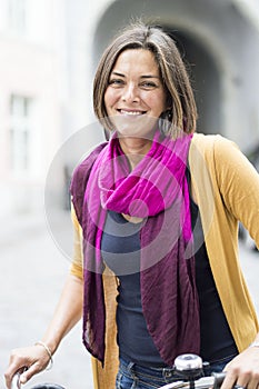 Smiling girl with the bike on the background of the city