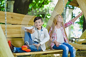 Smiling girl and boy having fun at playground. Children playing outdoors in summer. Teenagers on a swing.