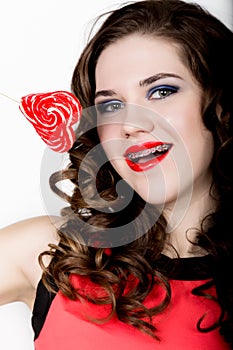 Smiling girl with braces holding heart candy posing on a white background