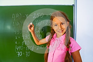 Smiling girl with braids and chalk near blackboard