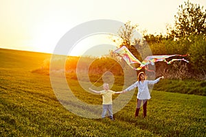 Smiling girl and brother boy standing and holding hands with flying colorful kites on the high grass meadow. Happy childhood